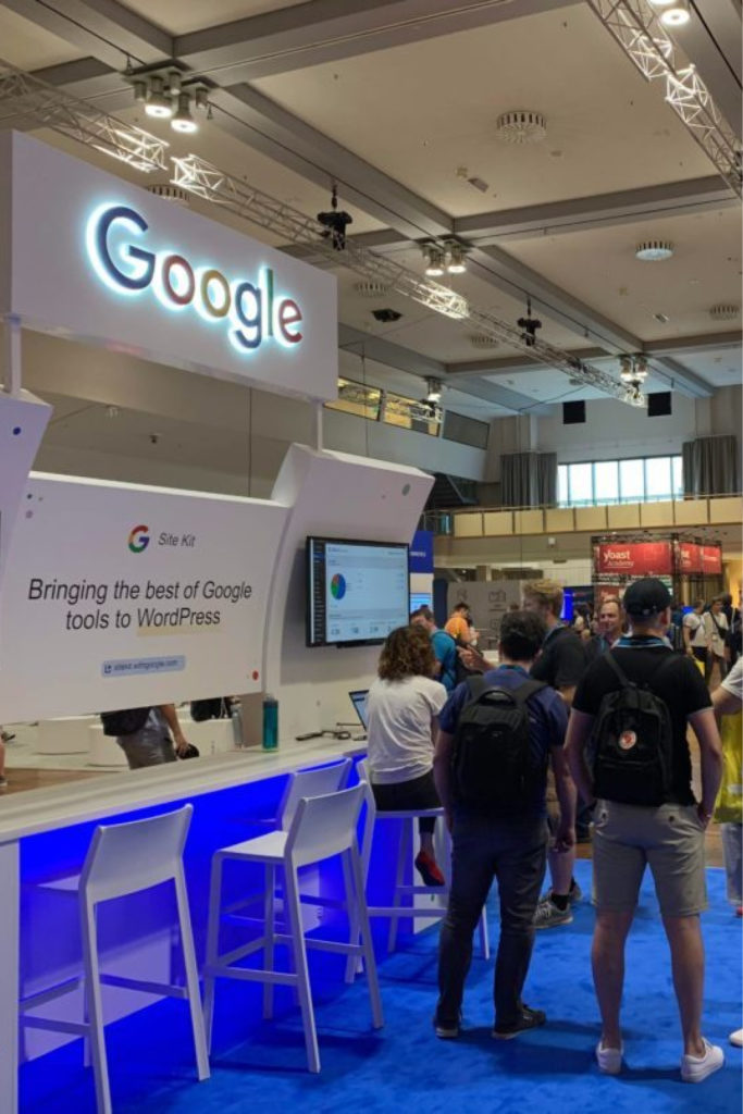 Google's conference booth at WordCamp Europe with people looking at a monitor displaying Site Kit's interface