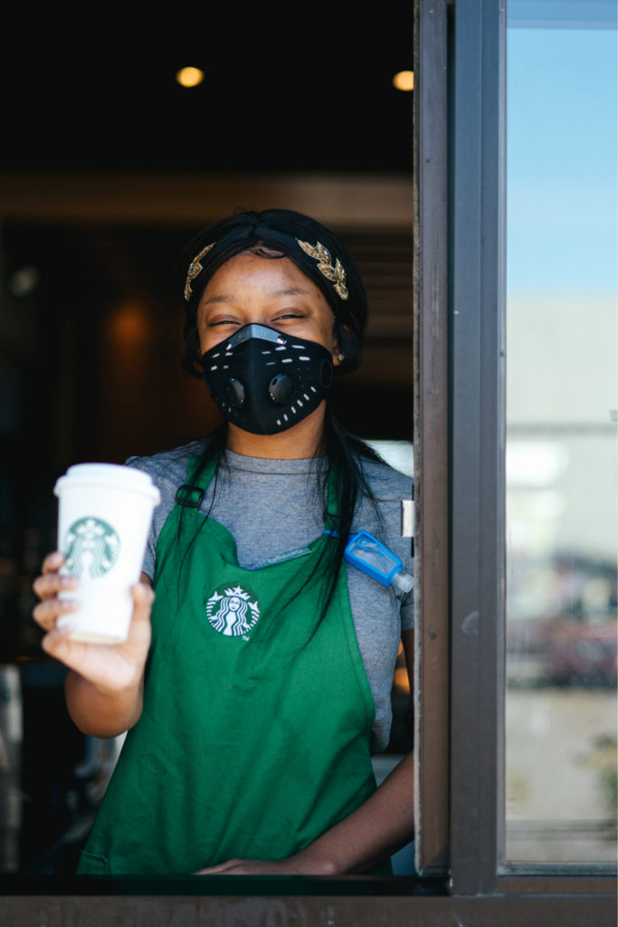 Starbucks barista wearing a face mask holding a drink cup at the drive through window